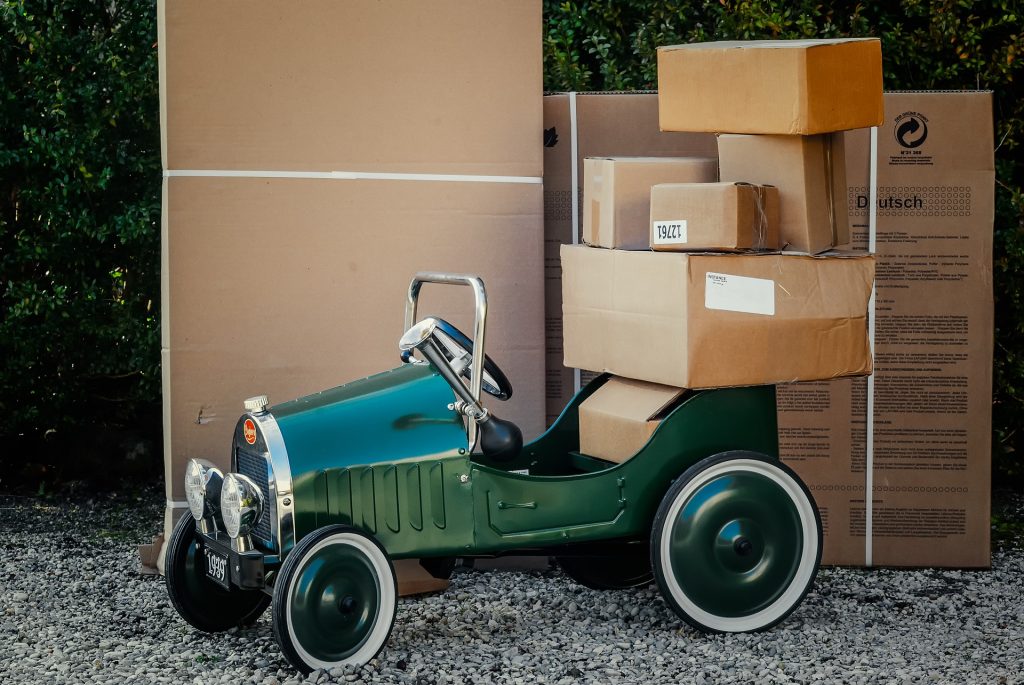 Cartons de déménagement empilés à l'arrière d'une petite voiture verte pour enfants et derrière